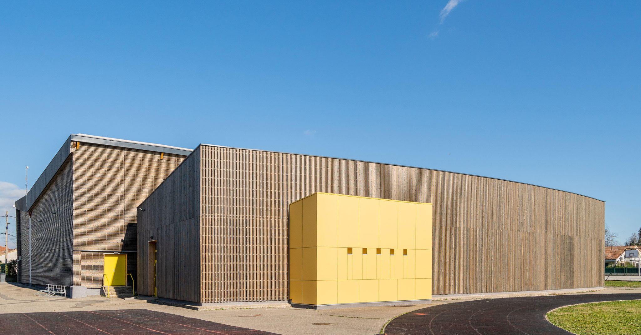 Gymnase Guy Pécoul rénové, façade en bardage bois et entrée jaune, sous un ciel bleu