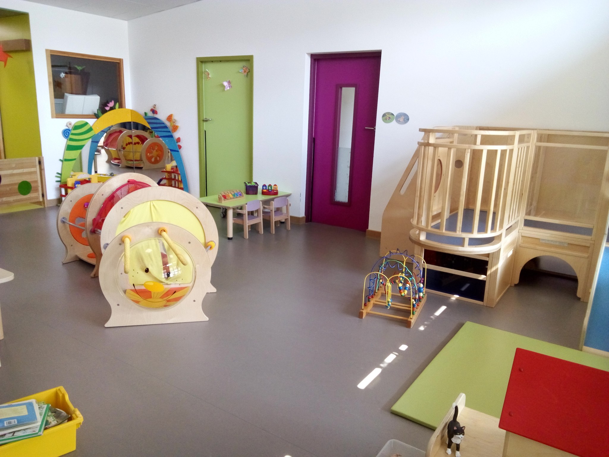 Salle de jeux de la crèche avec des arches de motricité, une structure en bois à escalier et de petites tables