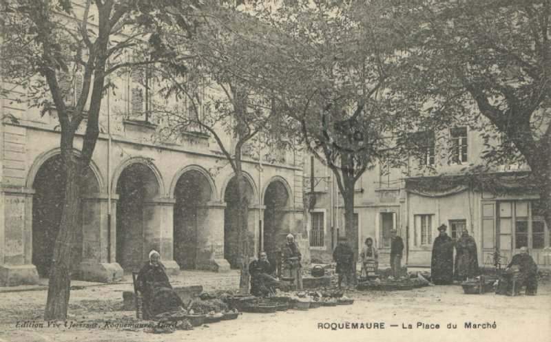 Carte postale ancienne « Roquemaure, la place du Marché » : arcades et platanes, marchandes assises près de leurs paniers posés au sol