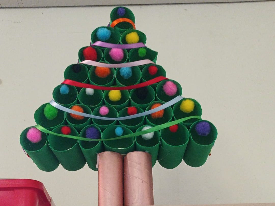 Sapin de Noël fabriqué avec des rouleaux de carton vert, décoré de pompons et de rubans de couleur