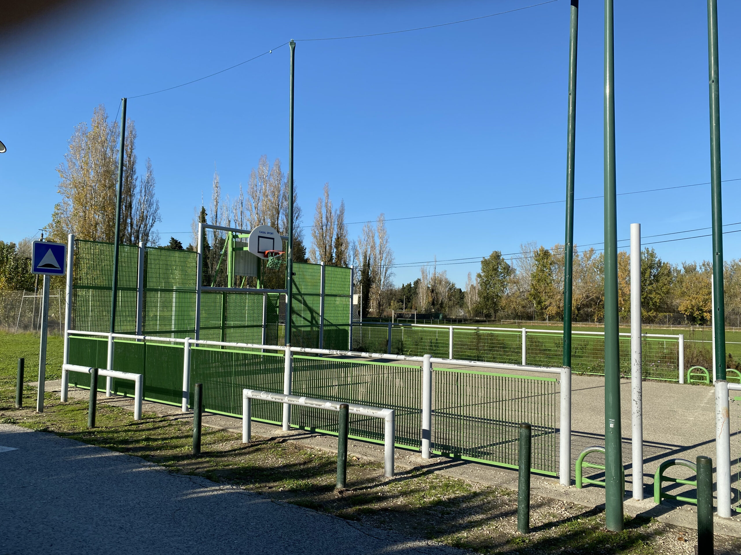 City-stade de l’île de Miémart : terrain clos de grillage vert avec panier de basket, au bord d’une allée