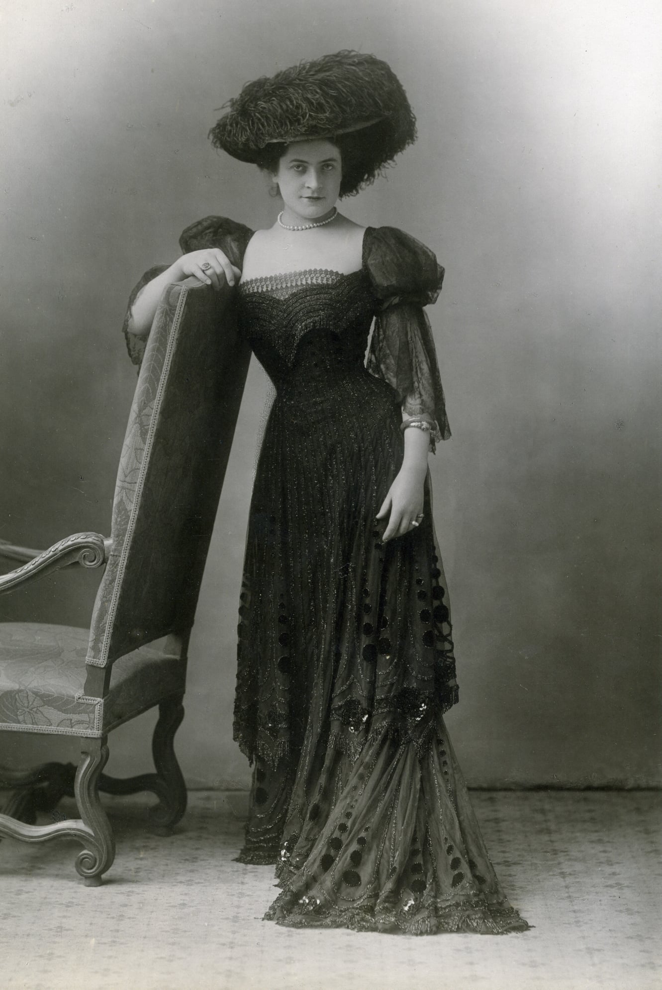 Photographie ancienne de la cantatrice Jeanne Hatto en robe longue et grand chapeau à plumes, accoudée au dossier d’un fauteuil