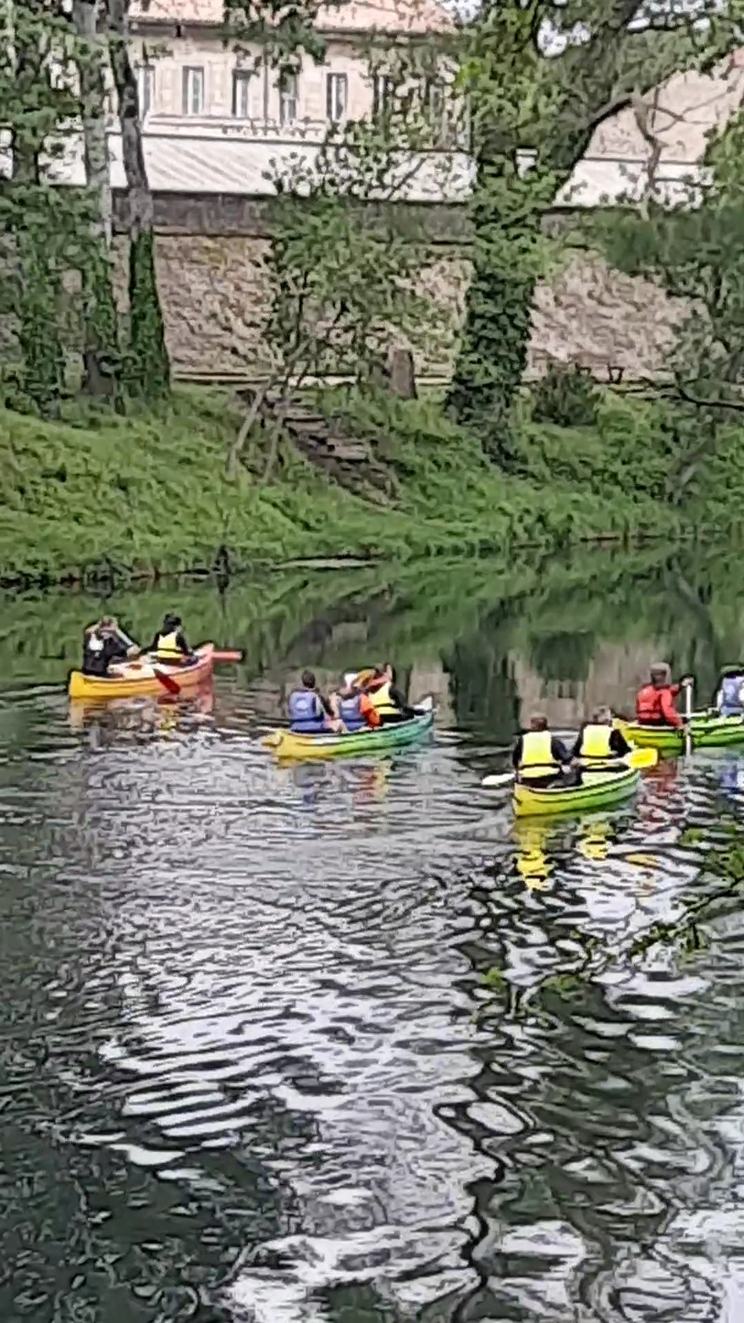 Groupe de canoës colorés sur l’eau calme de la lône, au pied d’une berge boisée et d’un haut mur de pierre