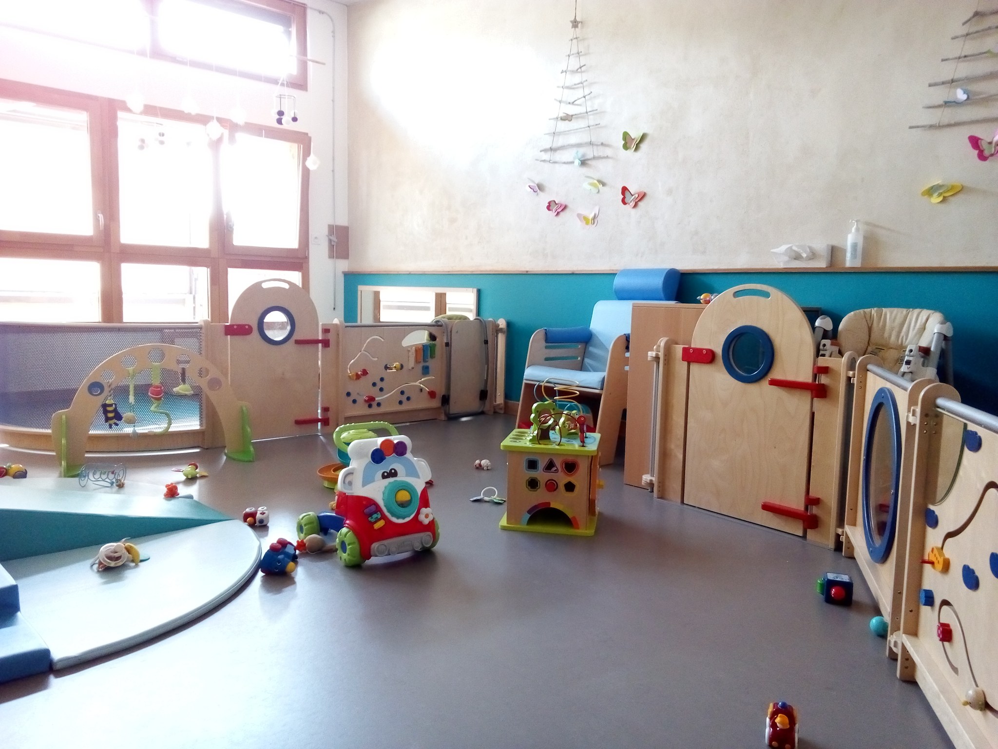 Salle de la crèche L’Auceloun : tapis de motricité, cloisons d’éveil en bois, chaise haute et jouets au sol