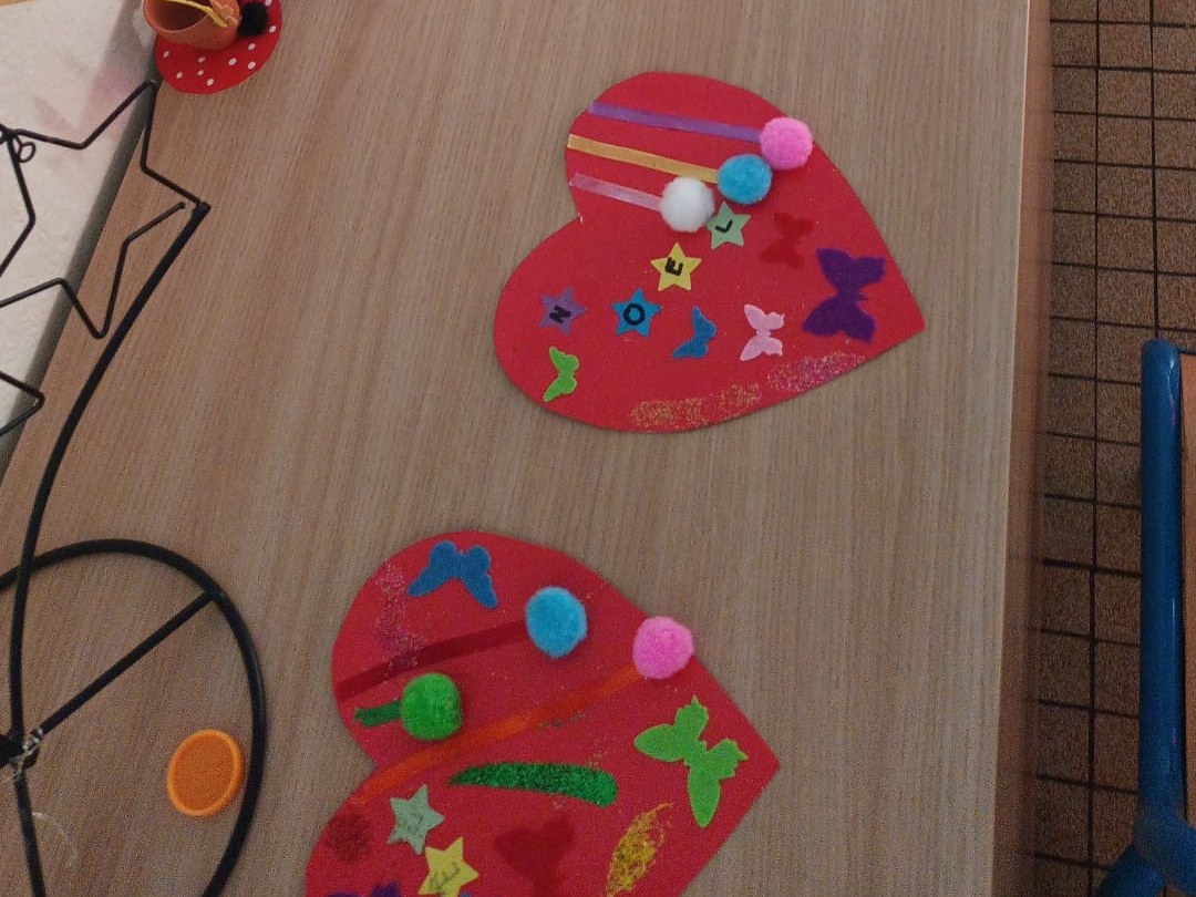 Cœurs en papier rouge décorés de pompons, de gommettes et de papillons, posés sur une table