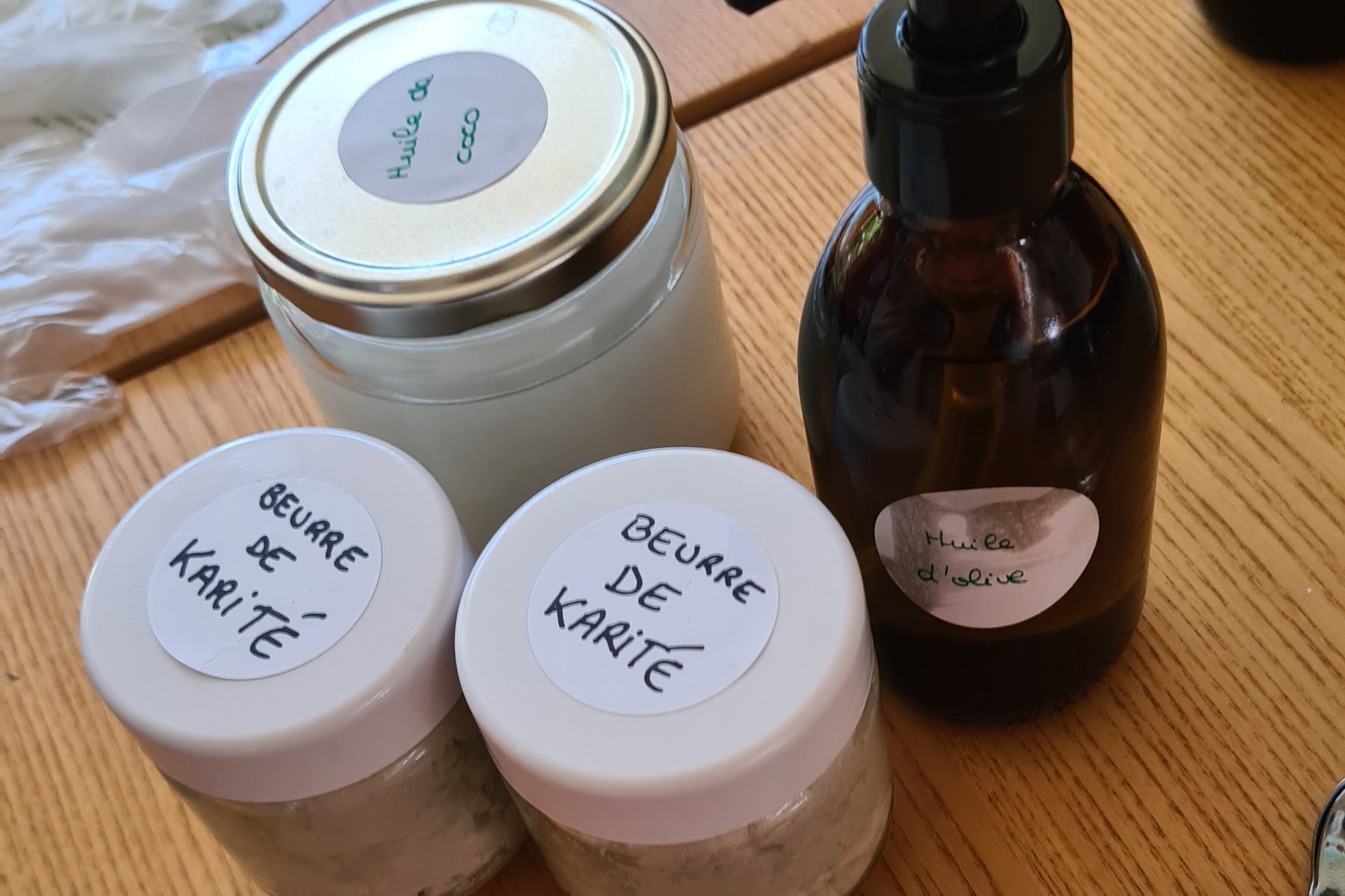 Pots étiquetés « beurre de karité » et « huile de coco » et flacon d’huile d’olive posés sur une table