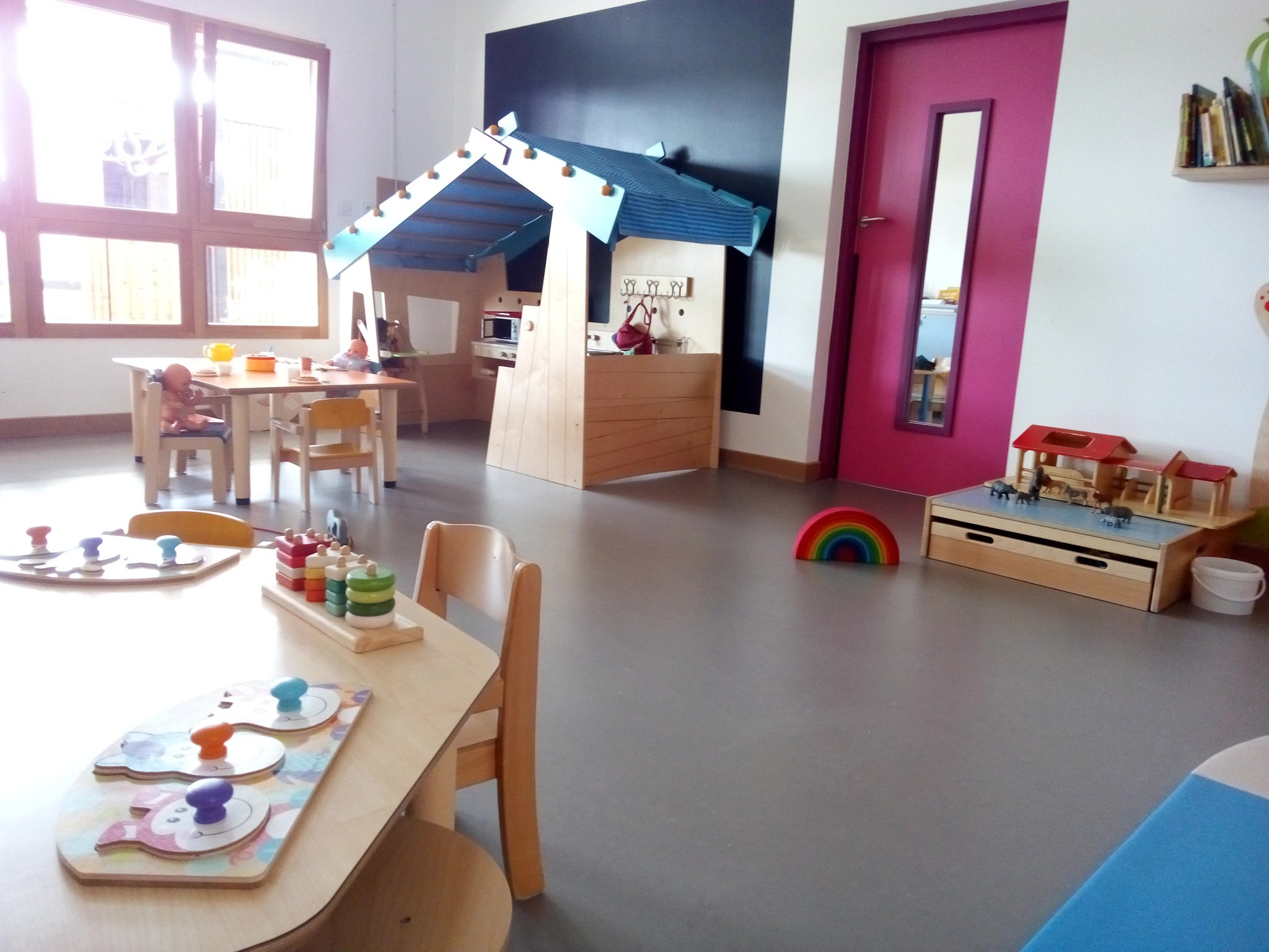 Salle de la crèche avec une maisonnette en bois, des tables basses, des chaises d’enfant et des jeux d’encastrement