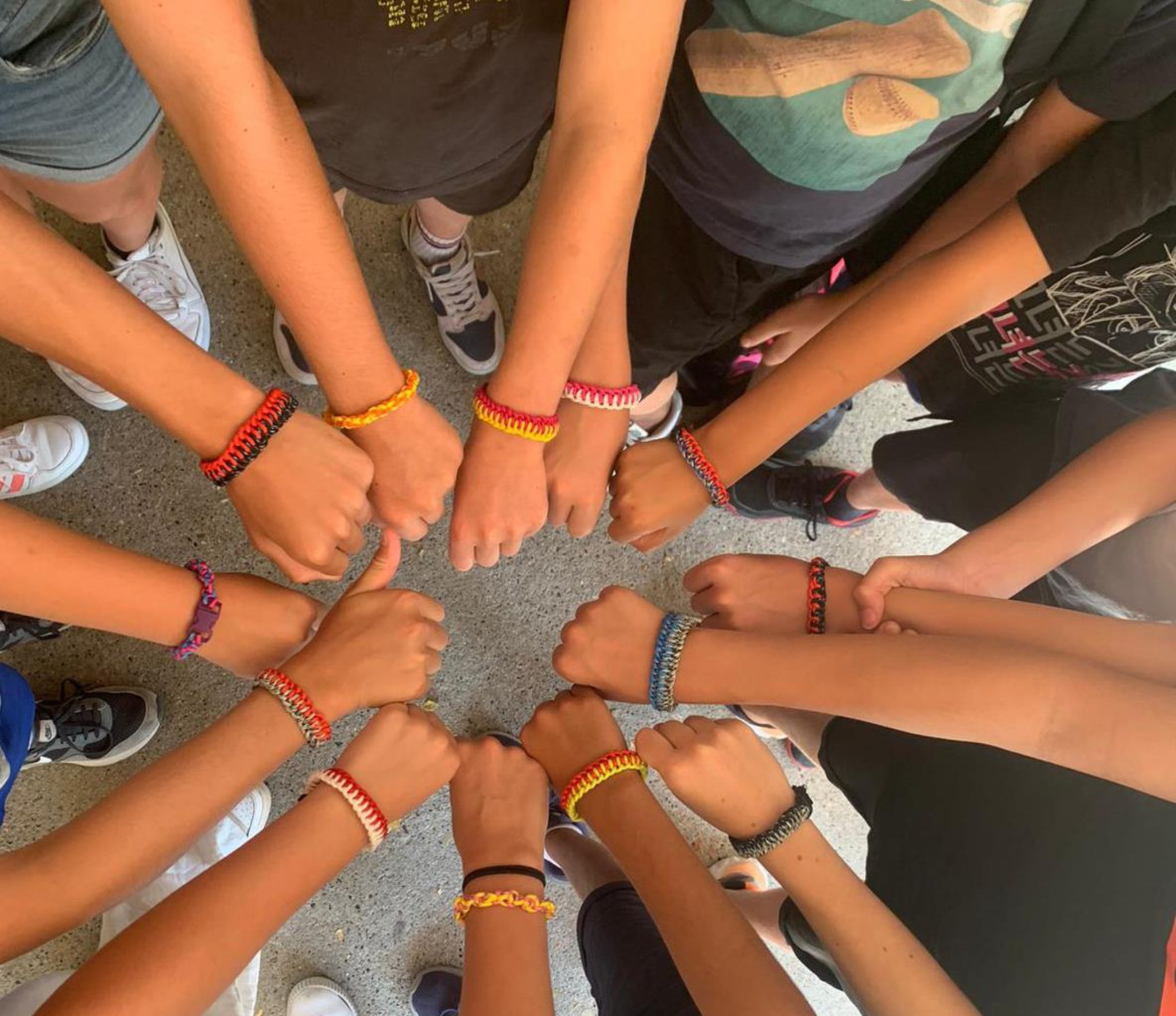 Poignets réunis en cercle, chacun orné d’un bracelet tressé de couleur