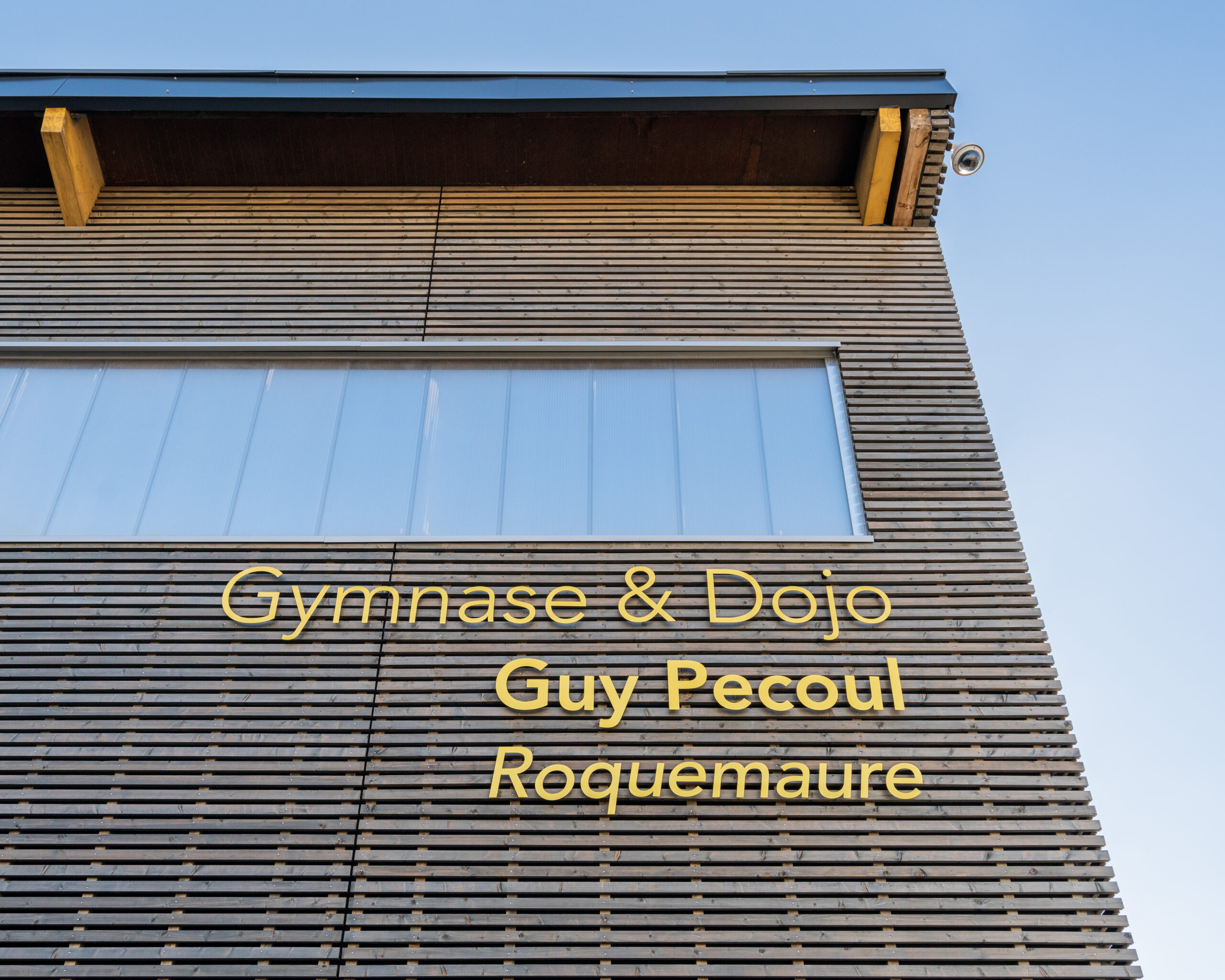 Façade en bardage bois du gymnase, avec l’inscription « Gymnase & Dojo Guy Pécoul Roquemaure »