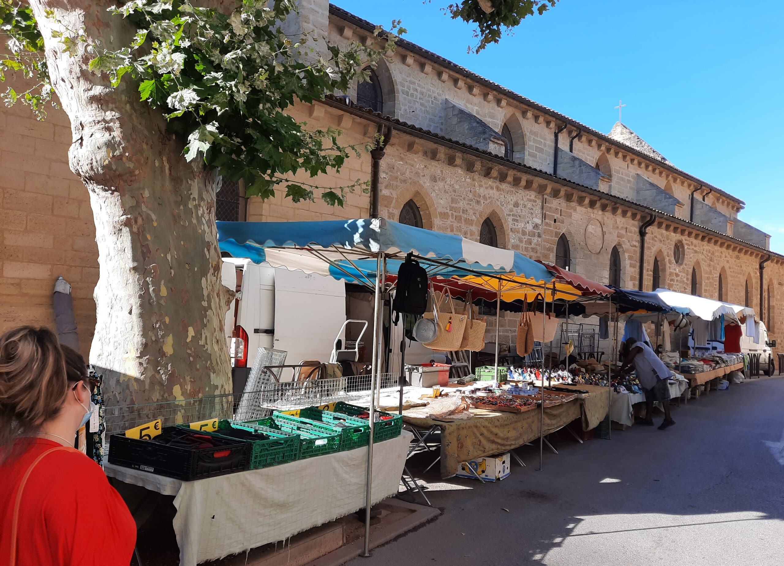 Rangée d’étals sous des parasols colorés, alignés le long d’un bâtiment en pierre aux fenêtres en arc