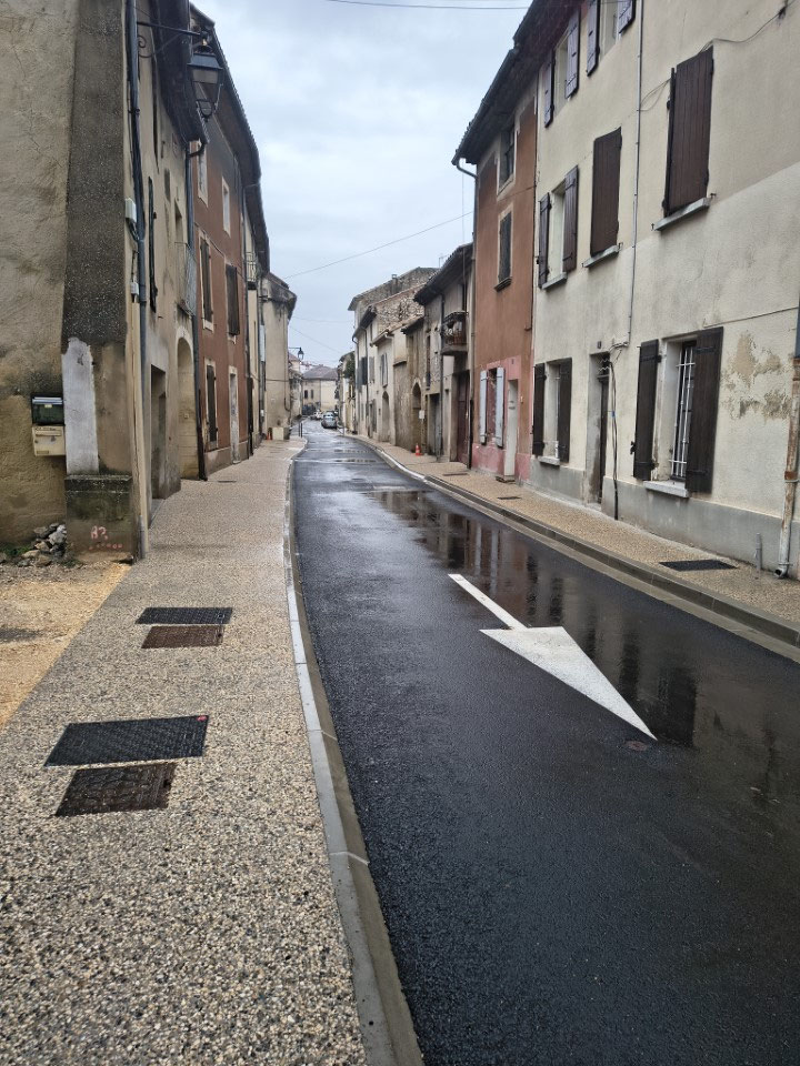 Rue étroite du centre ancien entre deux rangs de maisons anciennes à volets, trottoir neuf et chaussée refaite