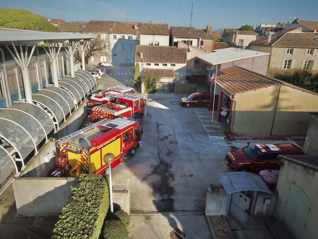 Vue plongeante sur la cour du centre de secours de Roquemaure, rue Carnot, avec ses camions de pompiers rouges sous l’auvent