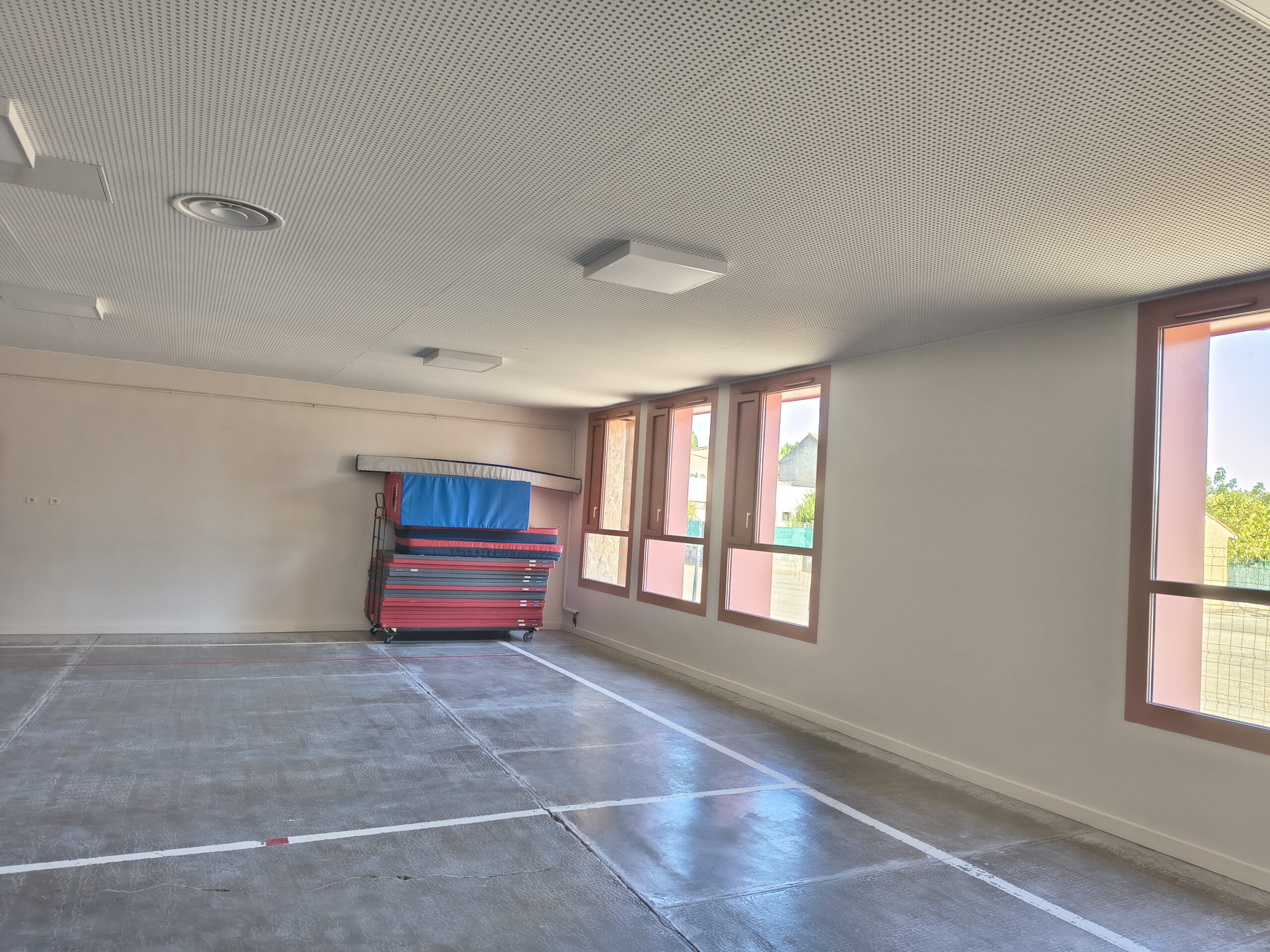 Le petit gymnase rénové, éclairé par de grandes fenêtres, avec des tapis de sport rangés au fond
