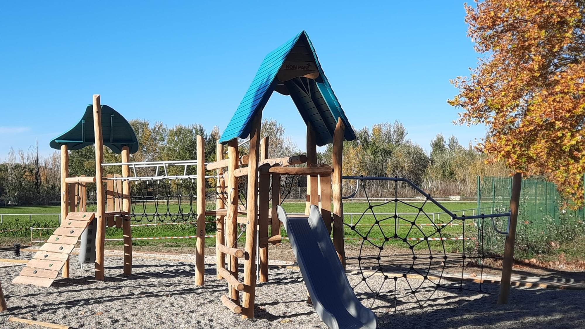 Aire de jeux de l’île de Miémart : structures en bois à toits verts, toboggan et filet à grimper sur le sable