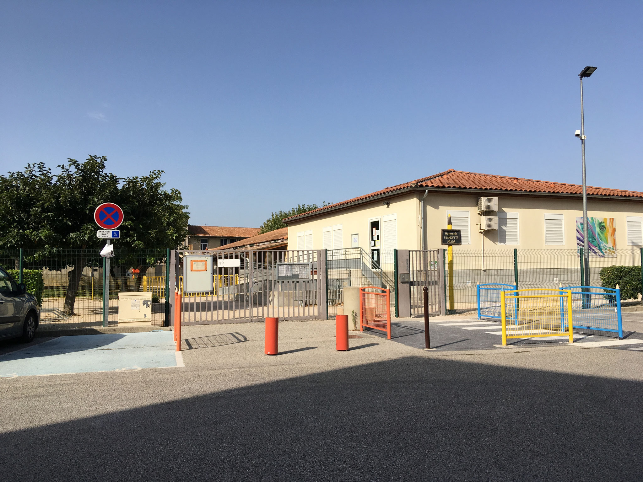 Portail et bâtiment de plain-pied de l’école maternelle, toit de tuiles, fresque colorée sur la façade
