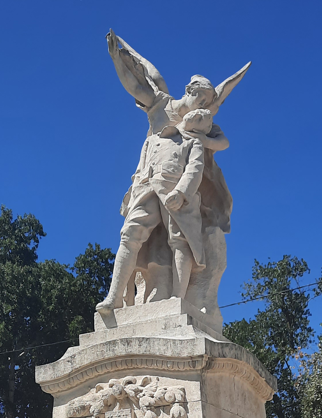 La statue du monument aux morts vue de près : la Patrie ailée soutenant le soldat tombé, sur fond de ciel bleu