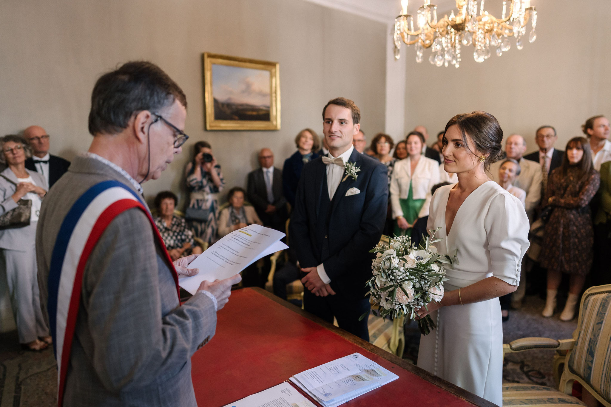 L’adjoint au maire, en écharpe tricolore, lit les articles du Code civil face aux futurs époux, dans la salle des mariages