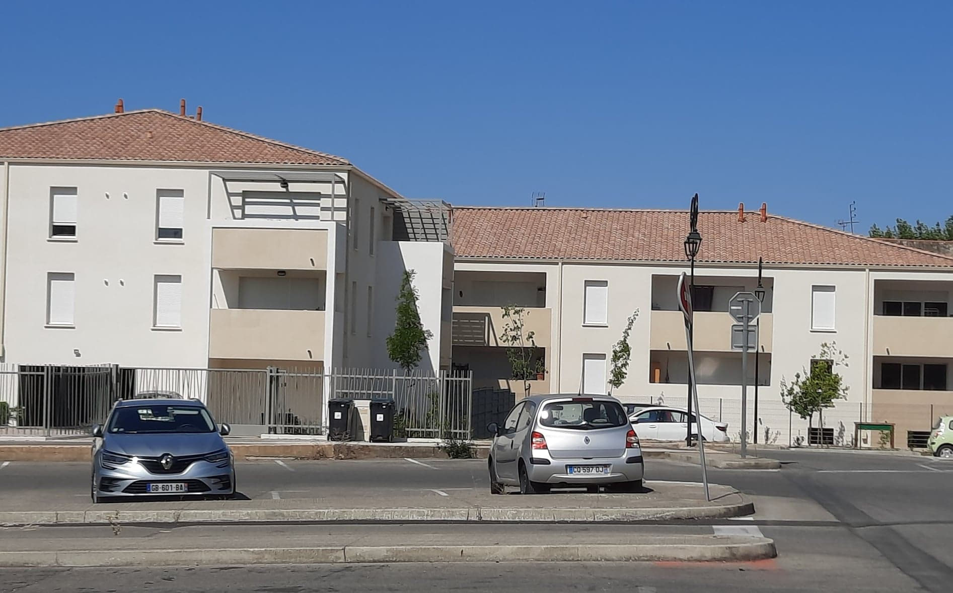 Résidence de deux étages aux murs blancs et toits de tuiles, avec loggias, vue depuis le parking