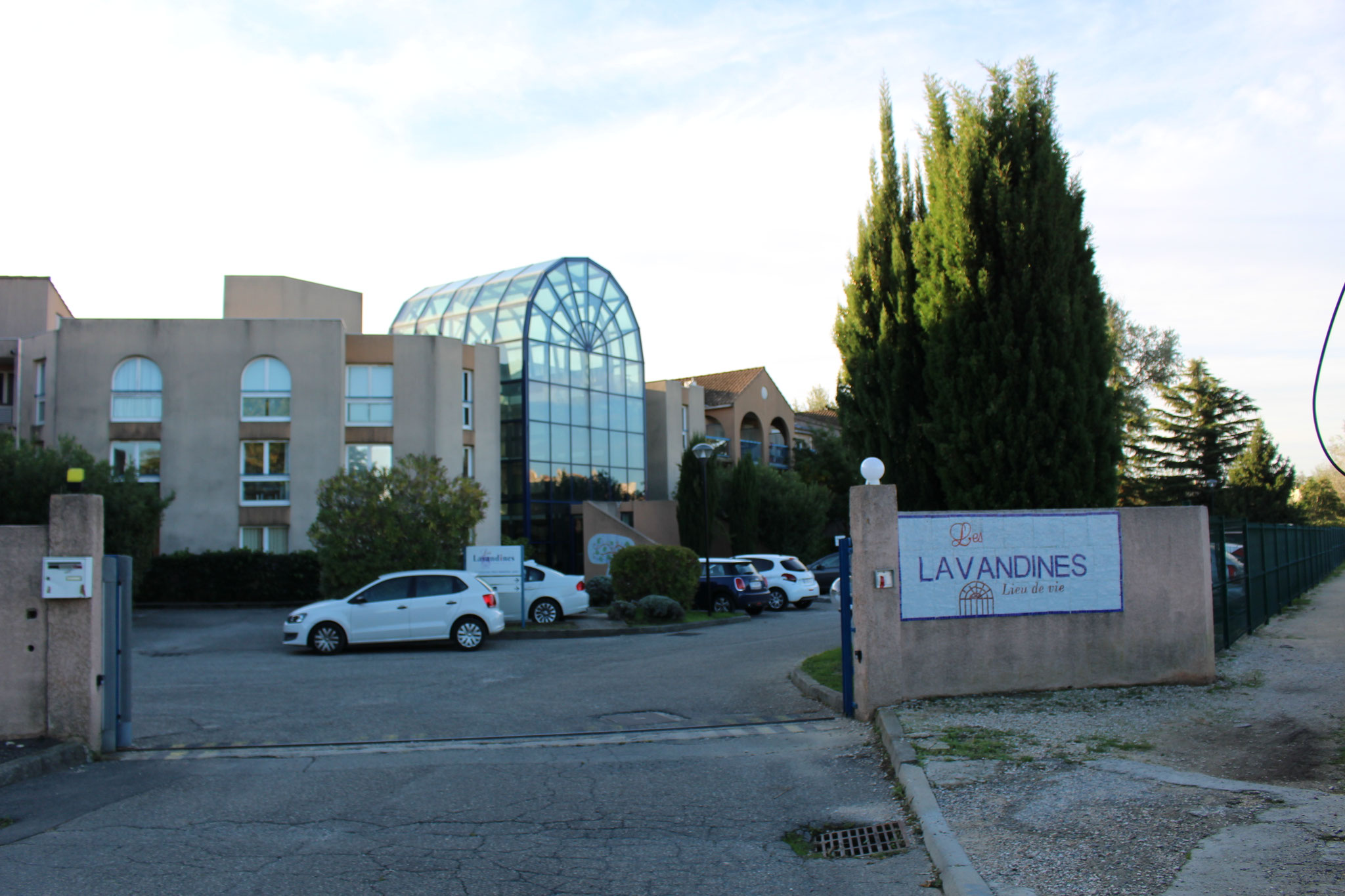 Entrée de l’EHPAD Les Lavandines : muret portant l’enseigne, cyprès, bâtiment à verrière arrondie