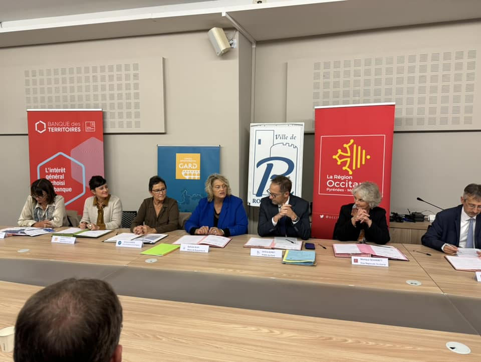 Élus et représentants des partenaires attablés pour la signature, devant les kakémonos de la Banque des Territoires, du Département du Gard, de la Ville et de la Région Occitanie