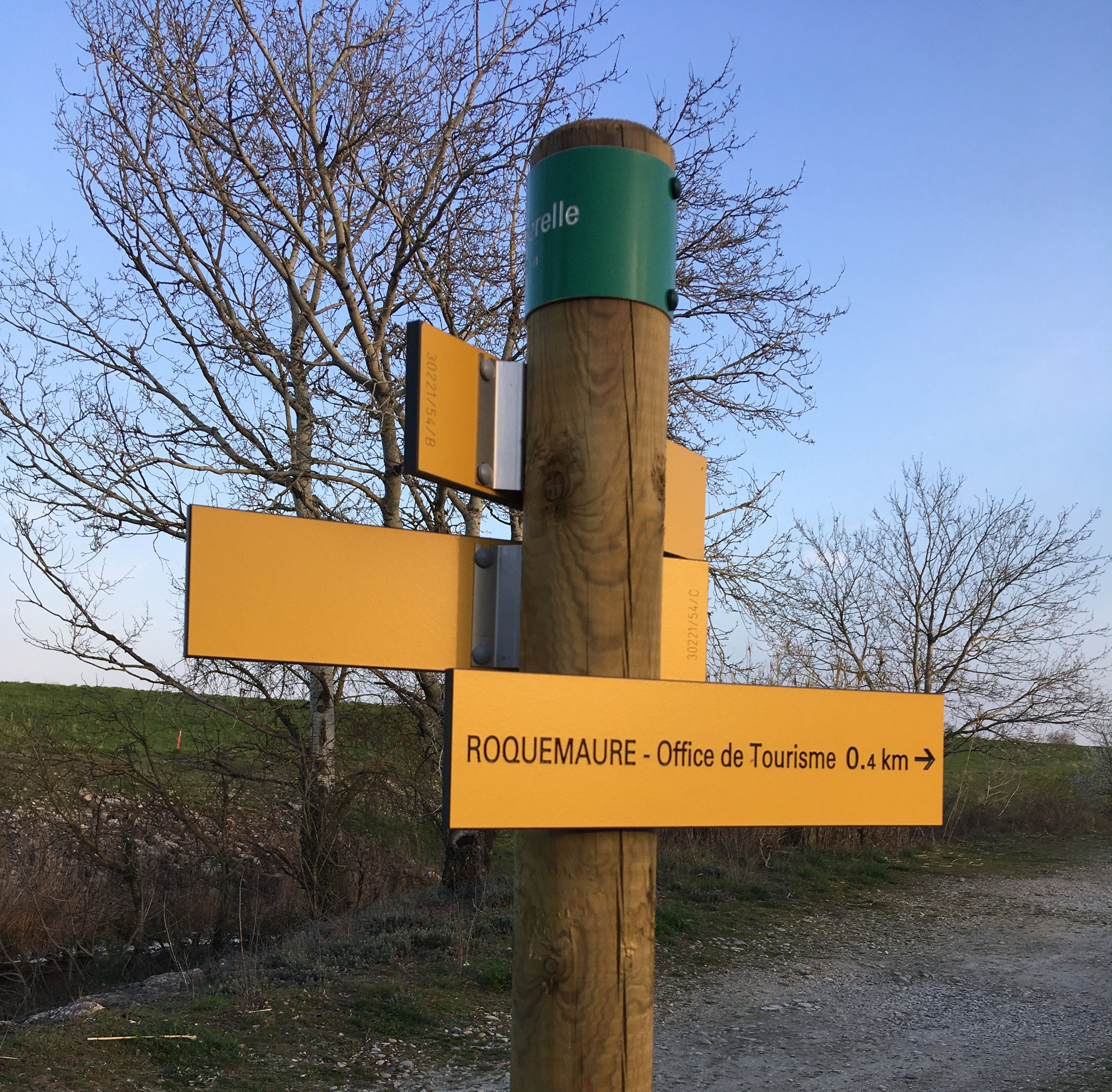 Poteau de balisage de randonnée avec ses lames jaunes, l’une indique « Roquemaure, Office de Tourisme 0,4 km »