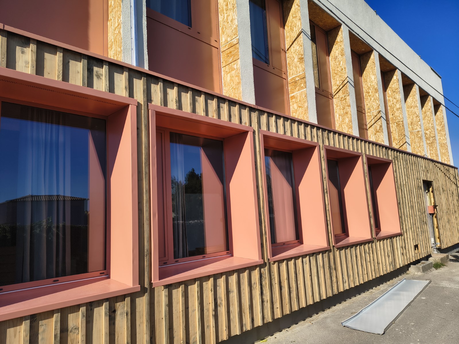 Façade du bâtiment Albert-Camus rénovée : bardage bois et encadrements de fenêtres saumon