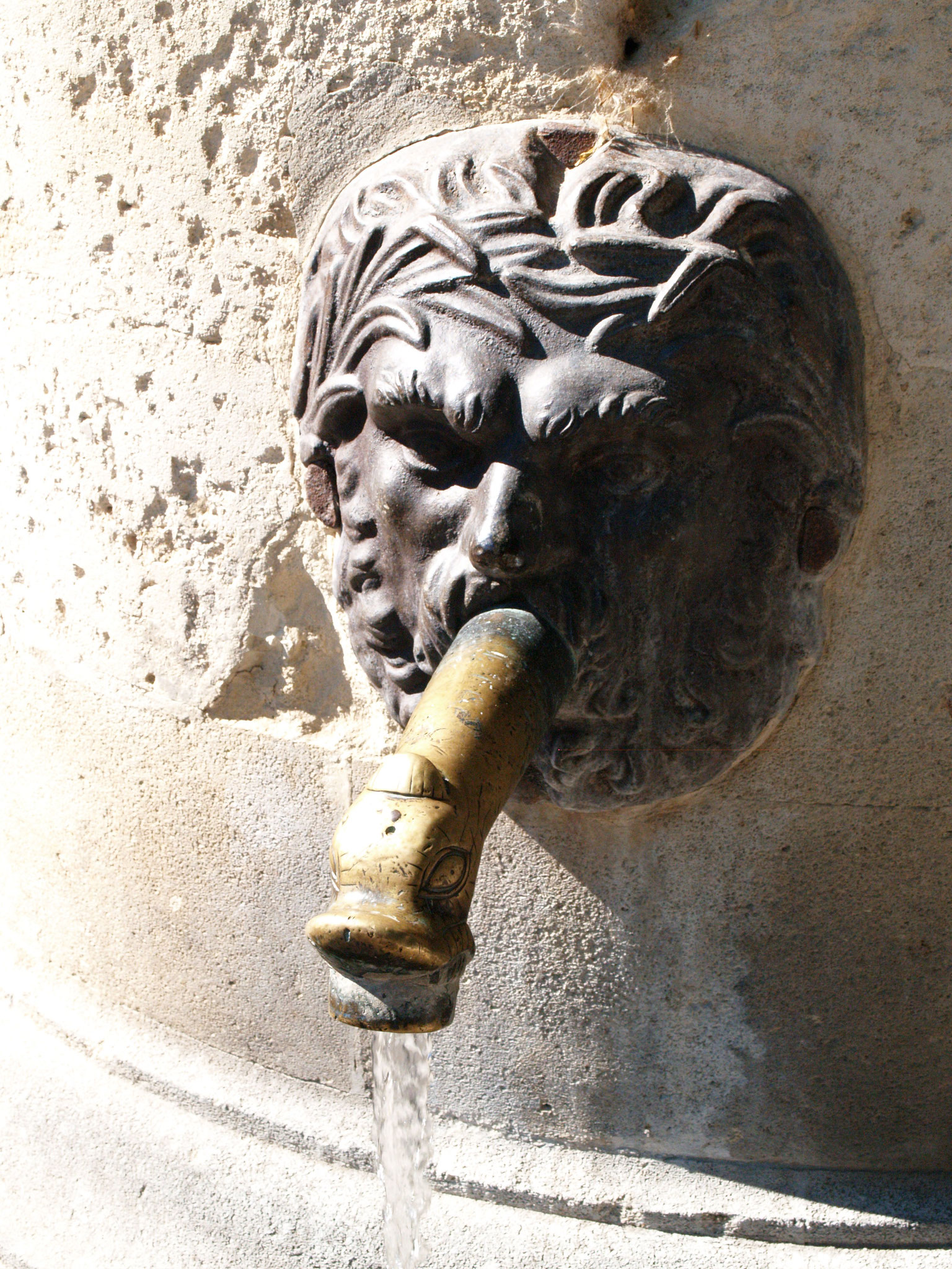 Visage sculpté dans la pierre, d’où sort un robinet de bronze