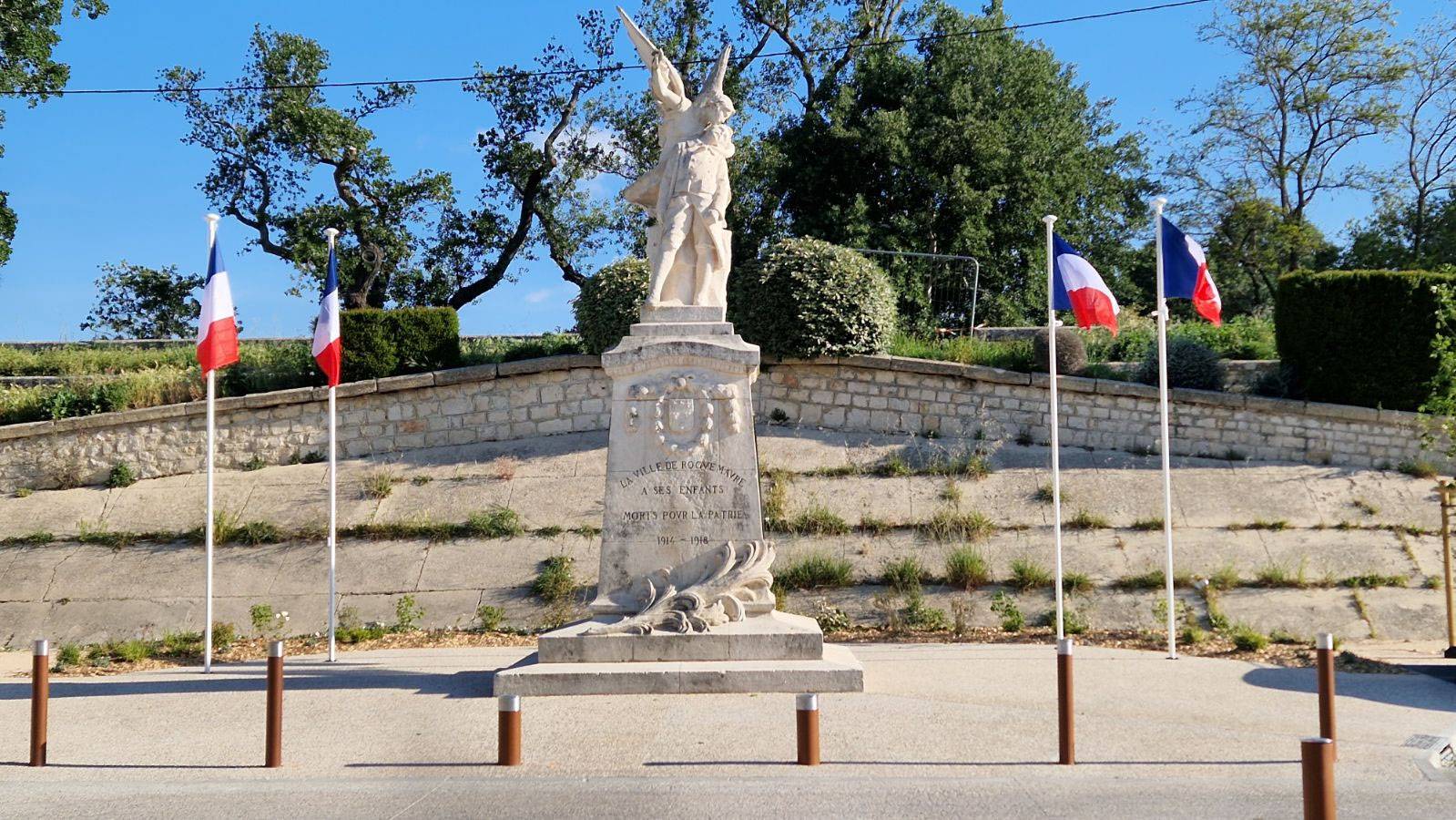 Le monument aux morts de Félix Charpentier, la Patrie ailée tenant le soldat tombé, sur son socle sculpté, entre des mâts aux drapeaux tricolores, esplanade Alphonse-Borrelly