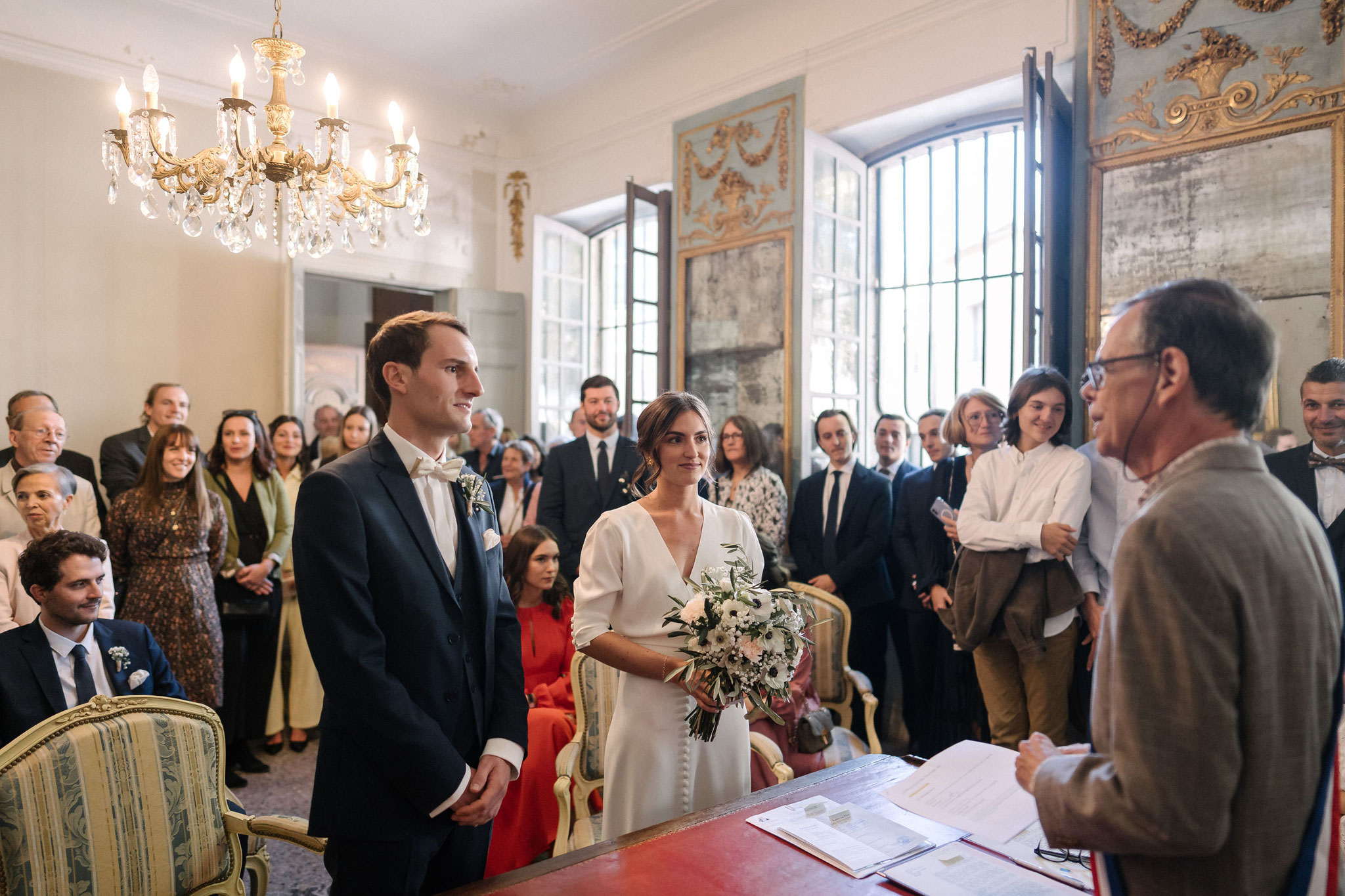 Dans la salle des mariages de l’hôtel de ville, les futurs époux debout devant la table de l’officier d’état civil, entourés de leurs invités