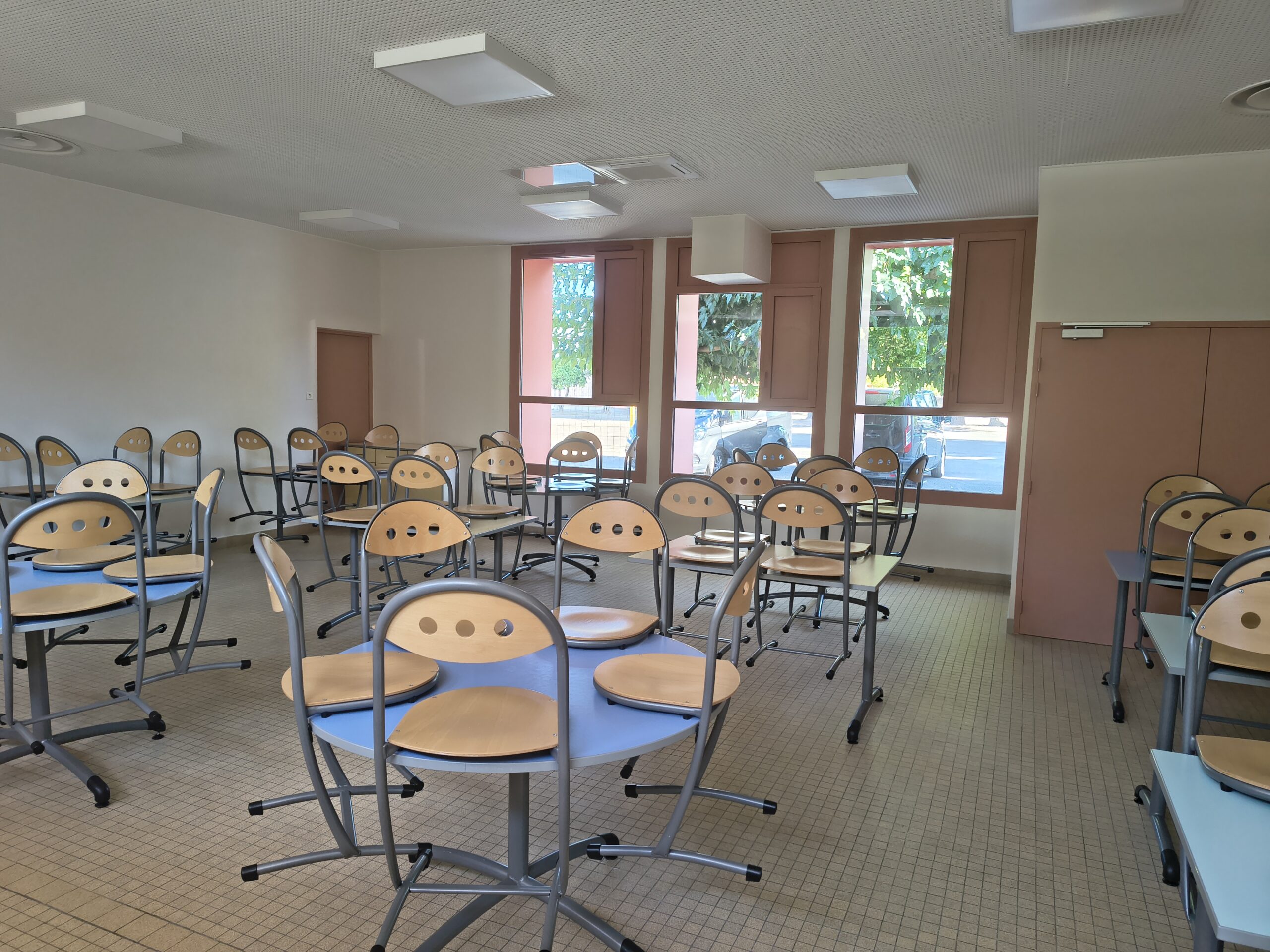 Salle de restauration rénovée de la cantine, tables rondes et chaises en bois clair