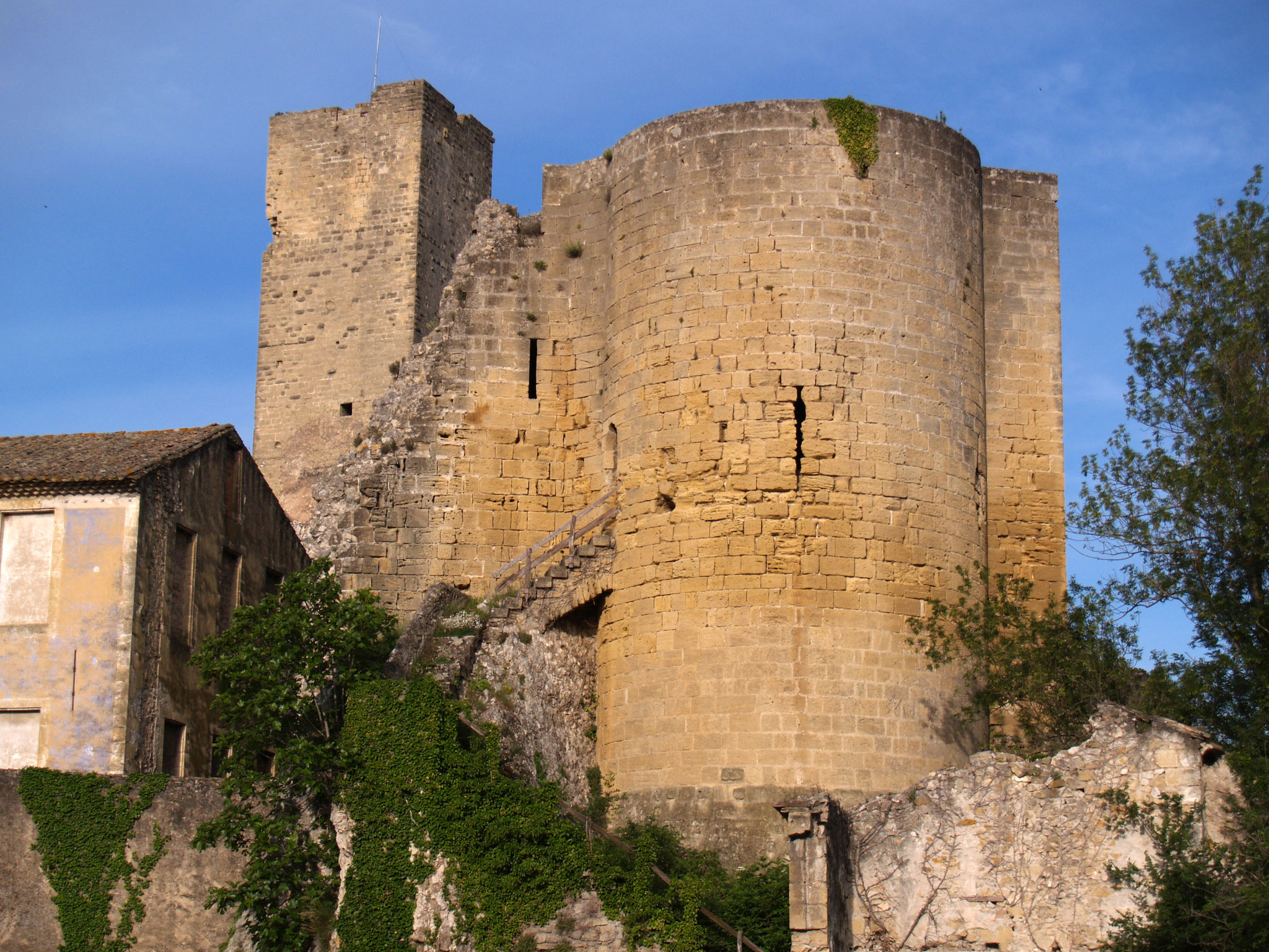 Ruines du château : une tour carrée et une grosse tour ronde en pierre dorée sous un ciel bleu