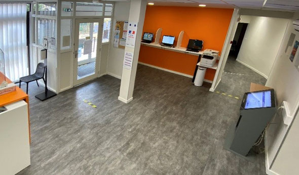 Le hall d’accueil de l’Espace CLIC : postes informatiques et imprimante le long d’un mur orange, borne tactile, porte vitrée d’entrée