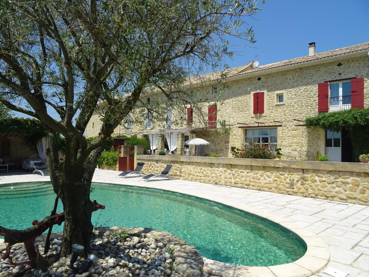 Grande maison de pierre aux volets rouges, piscine et olivier au premier plan